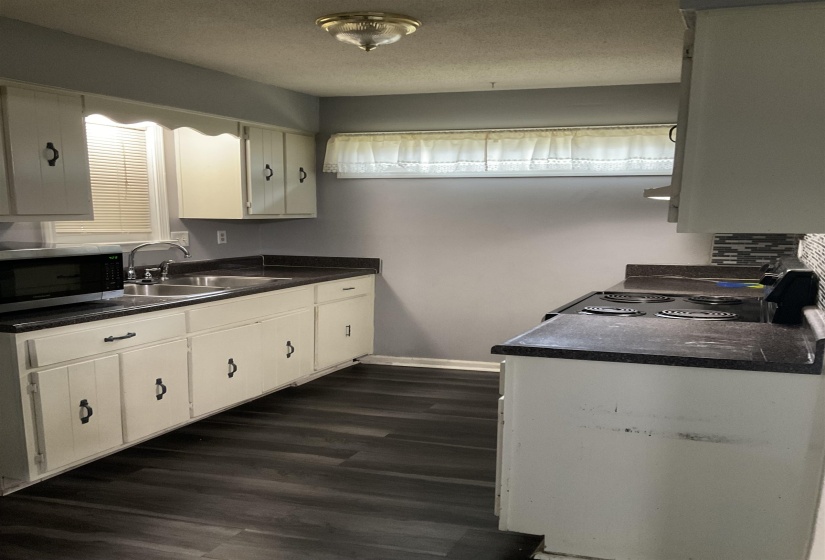 Kitchen featuring wood-finish flooring, white cabinetry, dark countertops, a double basin sink, and a built-in range