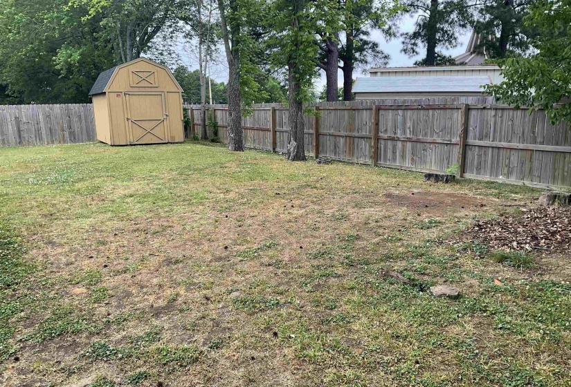Fenced backyard featuring a detached storage shed with a gambrel roof and double doors, mature trees, and a wooden privacy fence