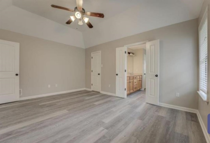Spacious room featuring wood-finish flooring, a vaulted ceiling with a ceiling fan, and neutral wall tones