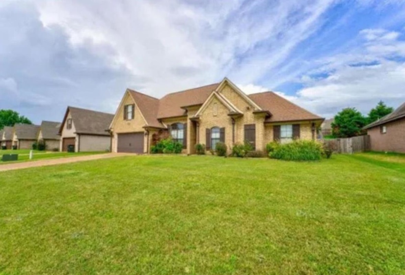 Brick exterior residence featuring a gabled roofline, front-facing garage, and established landscaping