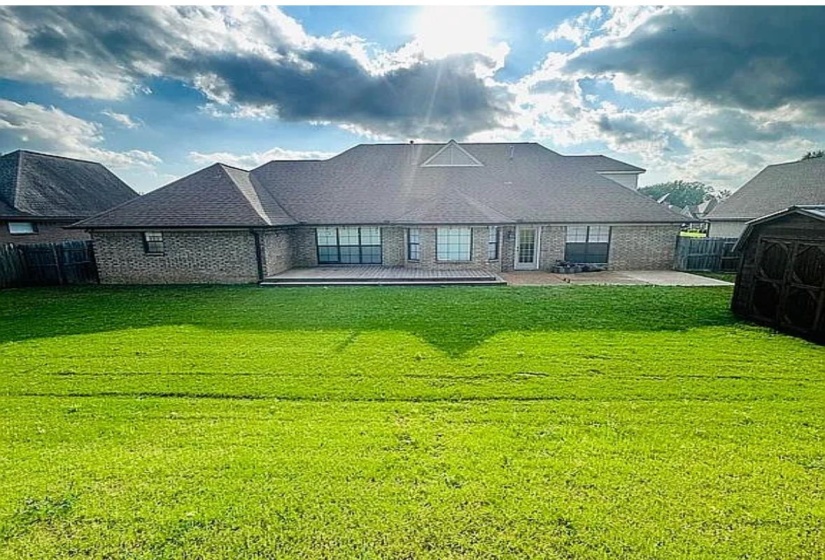 Spacious backyard featuring an extensive lawn, a multi-level patio, and a brick exterior with multiple windows