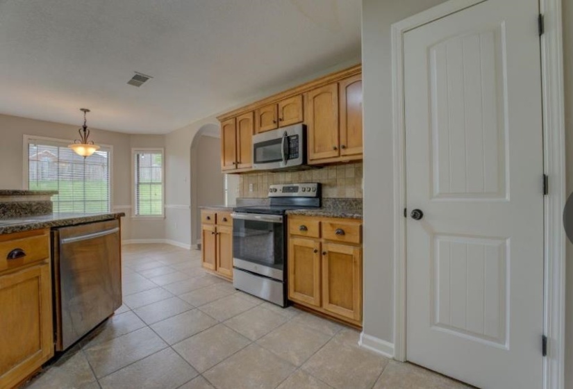 Kitchen featuring tile flooring, wood cabinetry, stainless steel appliances, and stone countertops