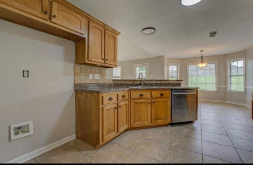 Kitchen featuring wood cabinetry, granite-look countertops, tile backsplash, stainless steel dishwasher, and tile flooring