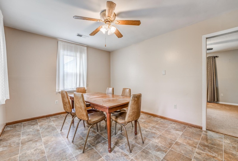 Dining area featuring patterned tile flooring, a window with sheer curtains, a ceiling fan with integrated lighting, and a doorway opening to an additional room