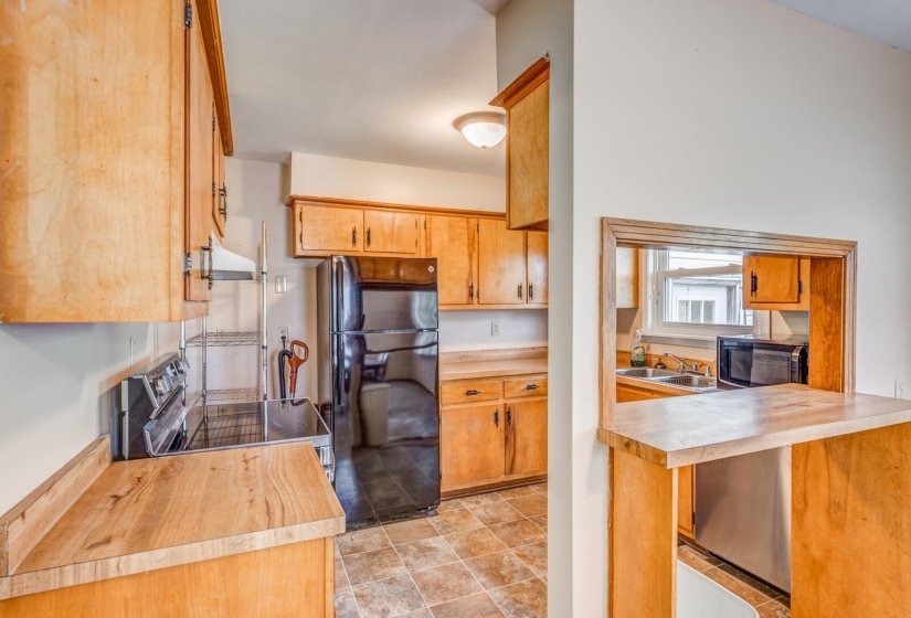 Kitchen featuring wood cabinetry, laminate countertops, a pass-through window, and durable tile-look flooring