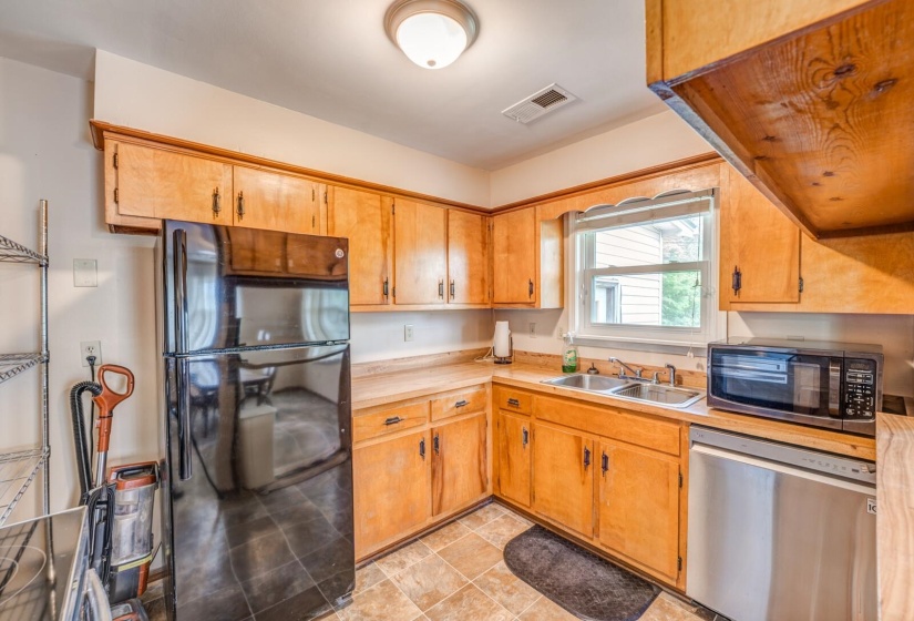 Functional kitchen featuring wood-finish cabinetry, a dual basin stainless steel sink, and a black refrigerator
