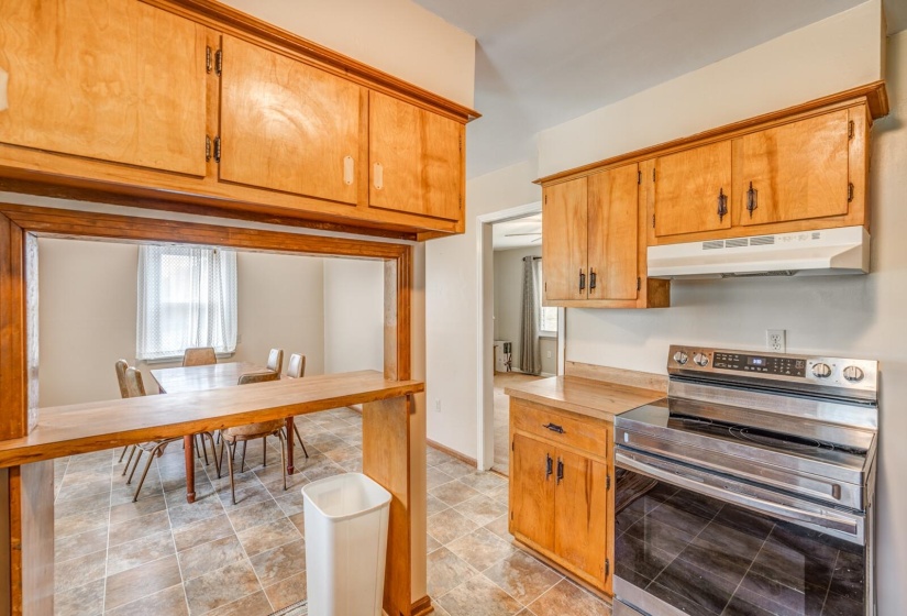 Kitchen featuring light wood cabinetry, a stainless steel range, and a pass-through window with a wood-finish countertop