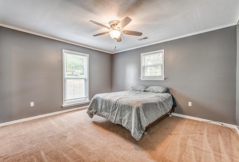Spacious room featuring neutral gray walls, crown molding, two windows with white blinds, and a ceiling fan with light fixture
