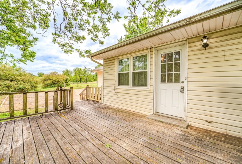 Exterior deck with wood railings, a white paneled door with windowpanes, and an exterior wall light fixture