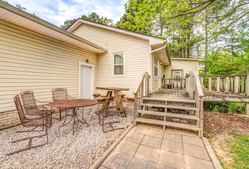 Exterior rear featuring beige siding, multiple entry points, a wooden deck with railing, and a stone paver pathway