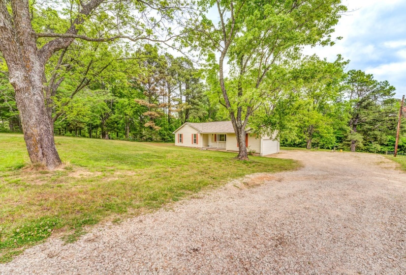 Ranch-style residence featuring a gravel driveway, mature trees, a covered front porch, and an attached garage