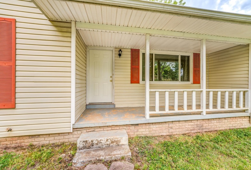 Covered porch entry featuring a paneled door, horizontal siding, and decorative red shutters
