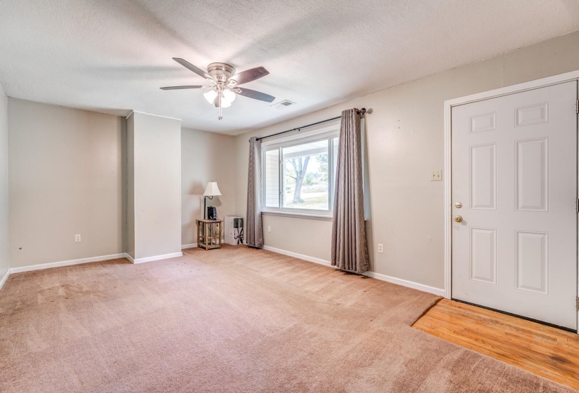 Spacious room featuring neutral paint, brown carpeting, a white paneled door, a window with exterior views, and a ceiling fan with integrated lighting