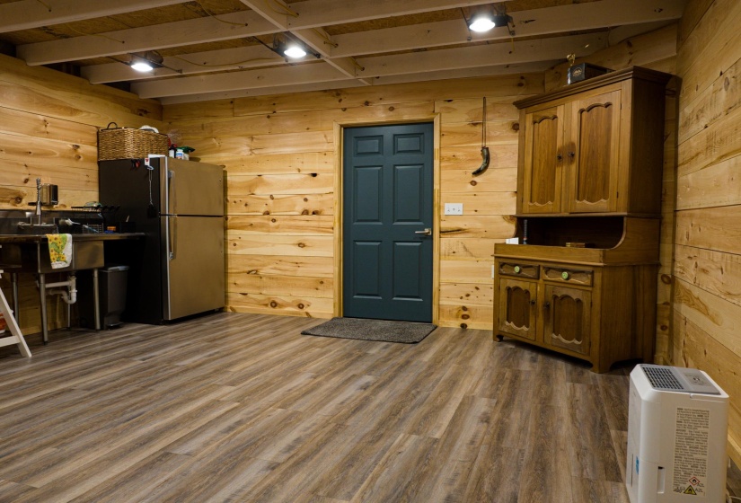 Wood-paneled room featuring wood-finish flooring, exposed ceiling beams, a dark-paneled door, recessed lighting, and a stainless steel sink with a dark countertop