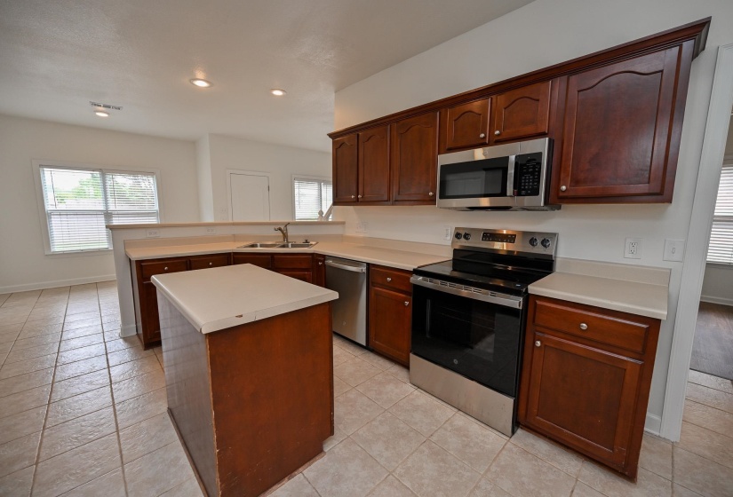 Kitchen featuring dark wood cabinetry, light-toned countertops, tile flooring, and stainless steel appliances including a range, dishwasher, and microwave