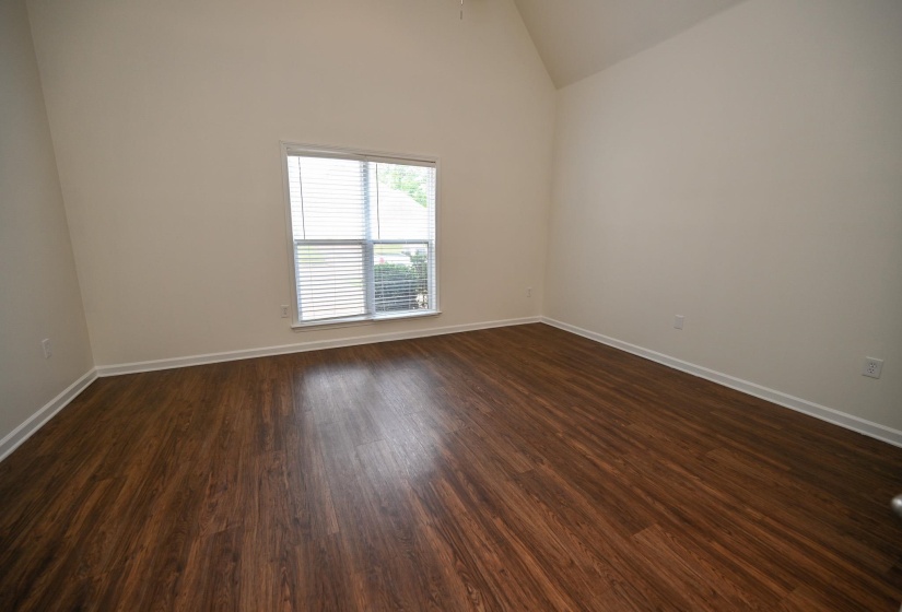 Room featuring a vaulted ceiling, wood-finish flooring, and a window with horizontal blinds