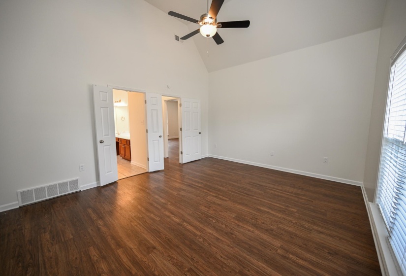 Spacious room featuring vaulted ceilings, wood-finish flooring, and a ceiling fan with integrated lighting