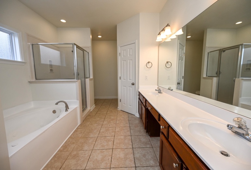 Spacious bathroom featuring a dual vanity with ample countertop space, a large wall-mounted mirror, a separate glass-enclosed shower, a built-in soaking tub, and tile flooring