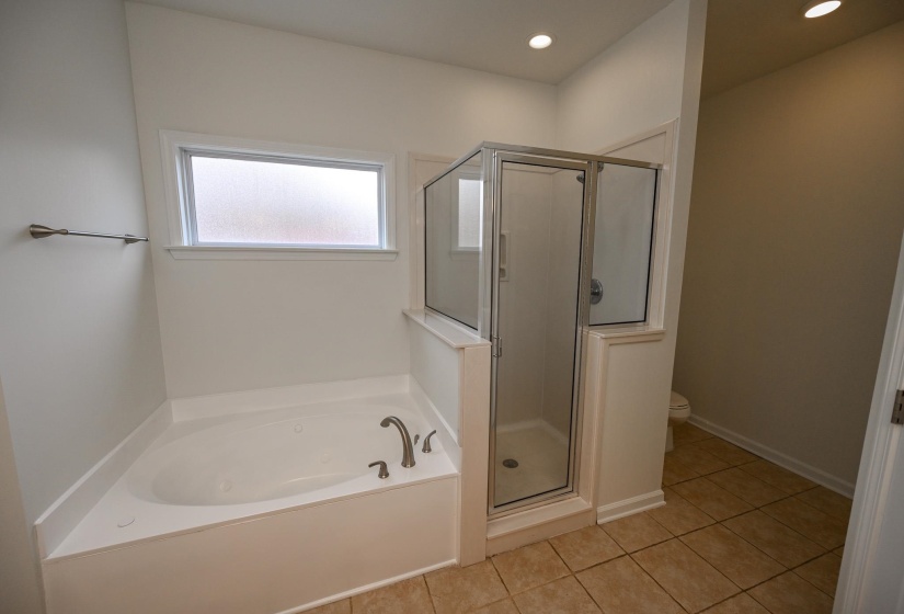 Corner soaking tub with brushed nickel fixtures, frosted window, glass-enclosed shower, recessed lighting, and tile flooring