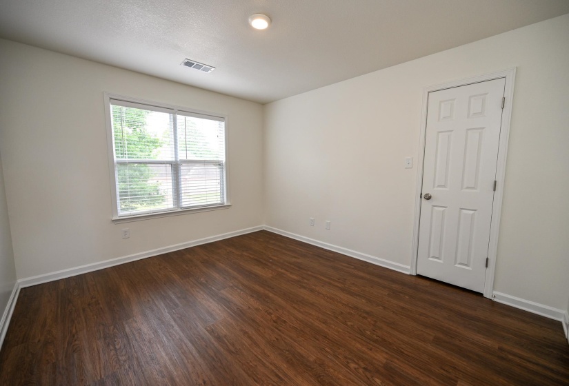 Bright interior room featuring wood-finish flooring, a multi-pane window with horizontal blinds, white baseboards, and a six-panel interior door with a brushed nickel knob