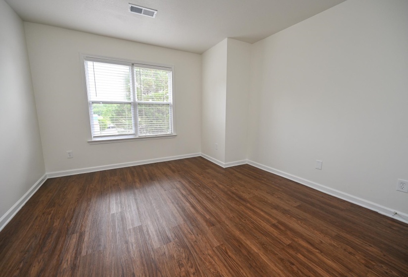 Light-filled room featuring wood-finish flooring, white baseboards, and a large window with blinds