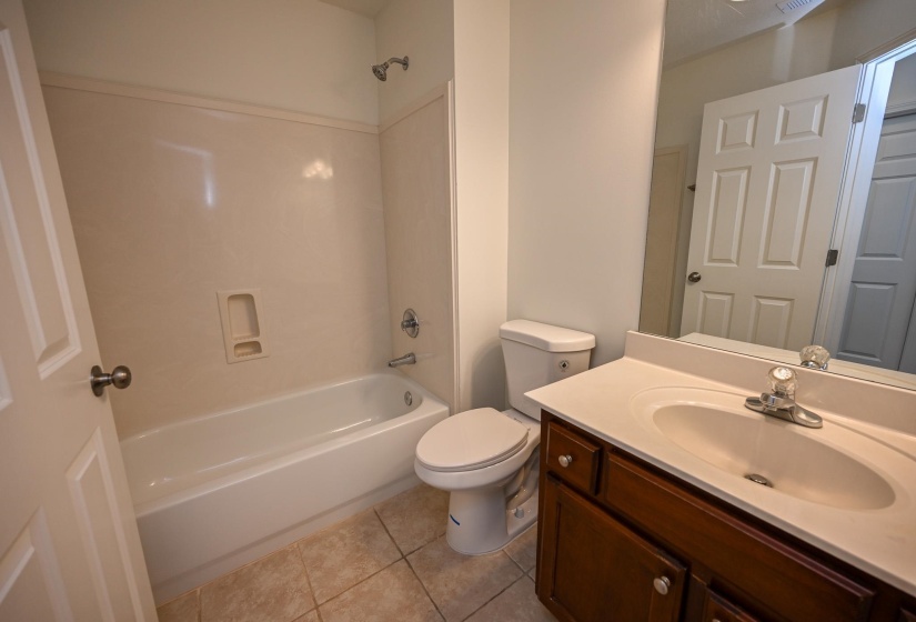 Bathroom featuring a white tub/shower combination, a toilet, and a vanity with a white countertop and wood-finish cabinetry