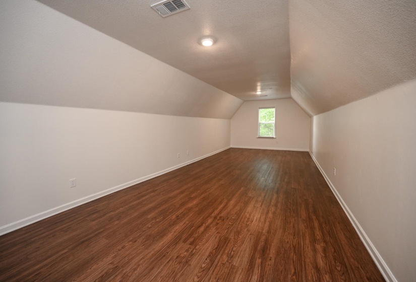 Spacious room featuring sloped ceilings, wood-finish flooring, and white baseboards