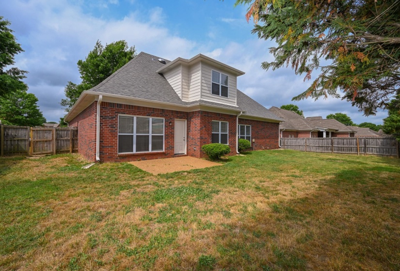 Rear exterior featuring a brick facade with a dormer, a patio, multiple windows, and a fenced yard