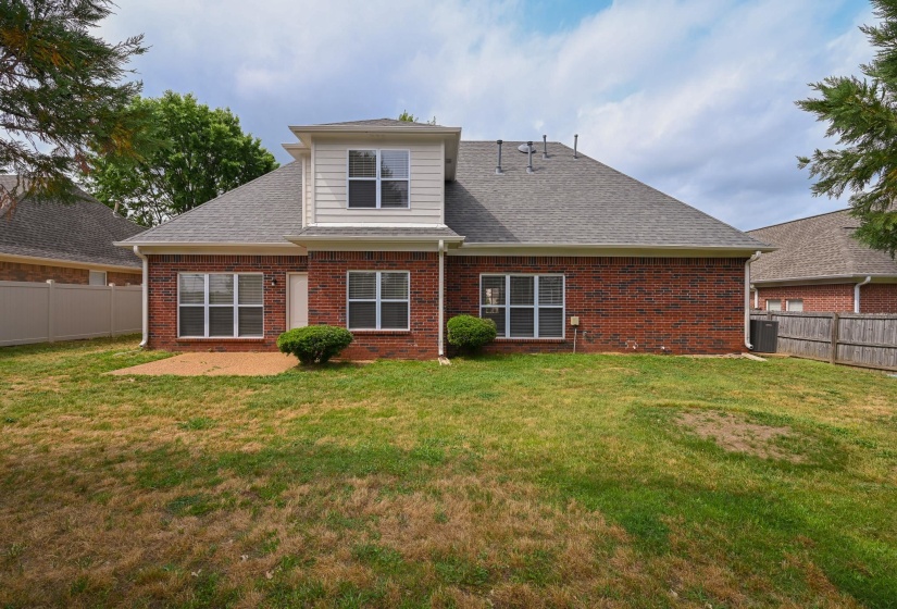 Rear exterior featuring brick and siding construction, multiple windows, a ground-level patio, and a shingled roof