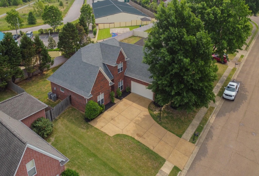 Brick exterior with a gray shingle roof, featuring a concrete driveway and mature landscaping
