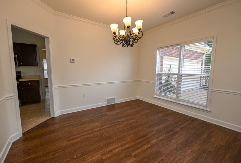 Spacious interior room featuring wood-finish flooring, a decorative chandelier, and a large window with blinds