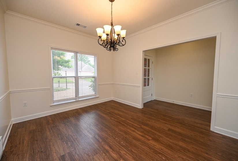 Spacious room featuring wood-finish flooring, a decorative chandelier, crown molding, and wainscoting