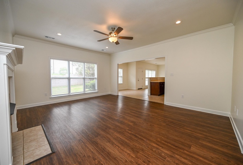 Spacious living area featuring wood-finish flooring, a white mantel fireplace with a tile hearth, and crown molding