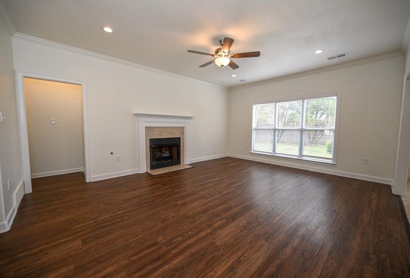 Spacious living area featuring rich wood-finish flooring, a classic fireplace with a tiled surround and white mantel, and ample natural light from multiple windows