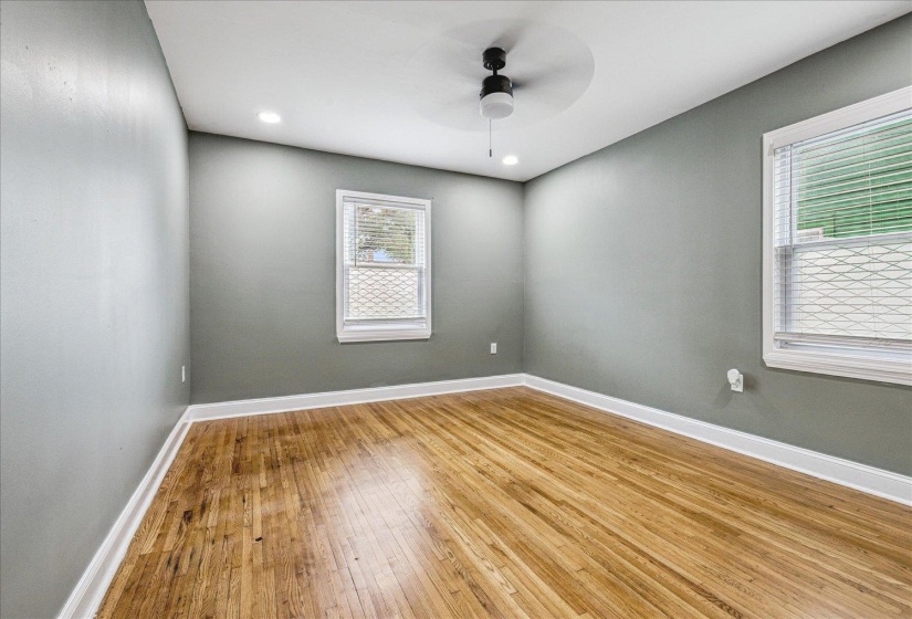 Spacious room featuring wood-finish flooring, two windows with blinds, recessed ceiling lights, a ceiling fan, and painted walls