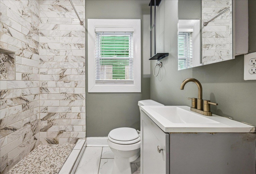Walk-in shower with subway tile surround and integrated niche, pebble-finish shower floor, white tile flooring, modern vanity with integrated sink, and bronze-finish faucet