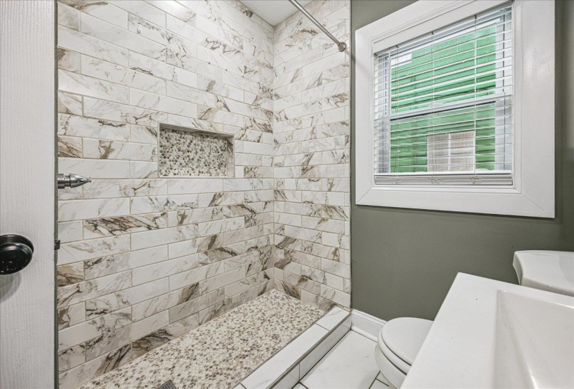 Shower featuring white and brown patterned subway tile walls, a built-in mosaic tile niche, and a contrasting mosaic tile shower floor