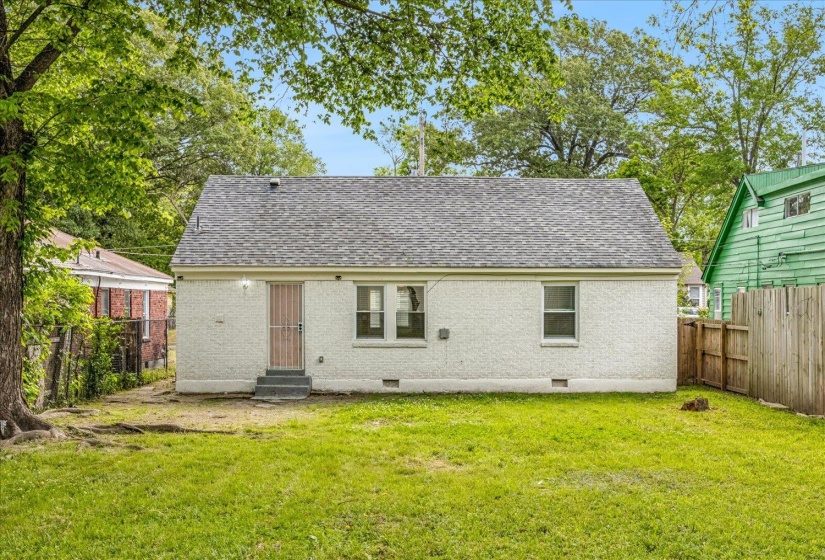 Rear exterior of the residence featuring a pitched roof with asphalt shingles, white stucco siding, and a security screen door