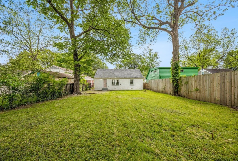 Expansive rear yard featuring a grass lawn, mature trees, and a privacy fence