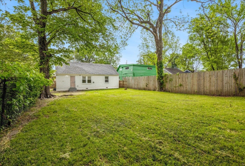 Expansive lawn area featuring a wooden privacy fence, mature trees, and a white exterior residence