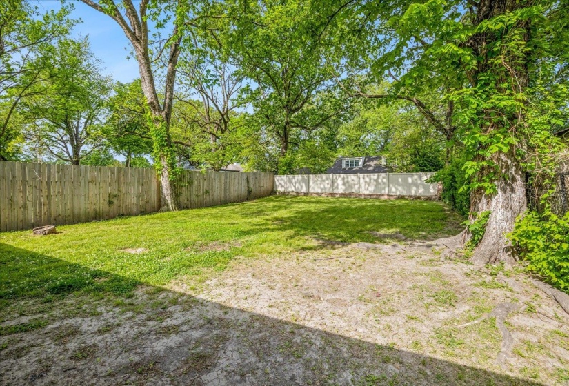 Expansive rear yard featuring mature trees, a wooden privacy fence, and a partially visible white fence