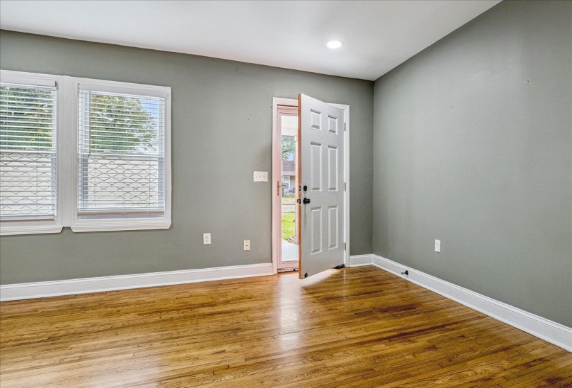 Interior room with wood-finish flooring, two large windows with blinds, a paneled door, recessed ceiling lighting, and light-toned wall paint