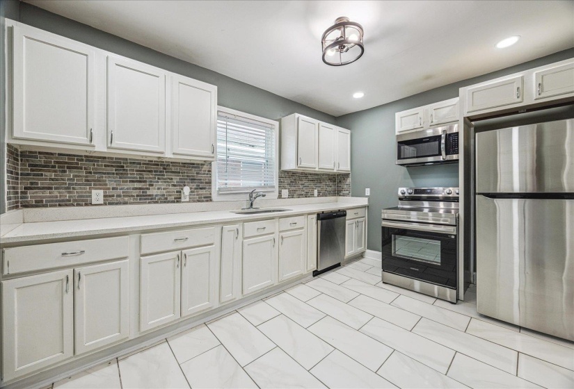 Kitchen featuring white shaker-style cabinetry, a mosaic tile backsplash, solid surface countertops, and stainless steel appliances
