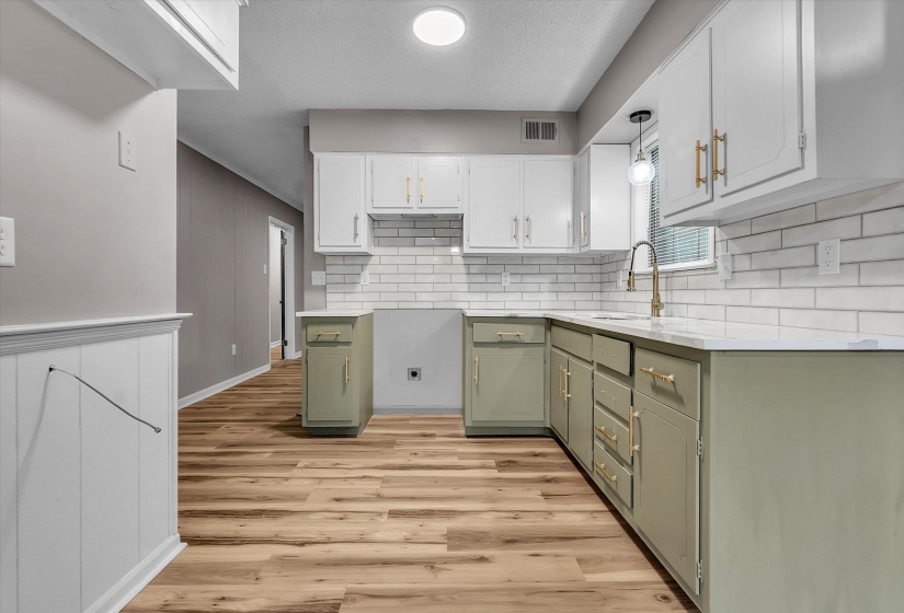 Kitchen featuring two-tone cabinetry with gold-tone hardware, white subway tile backsplash, and light-tone countertops