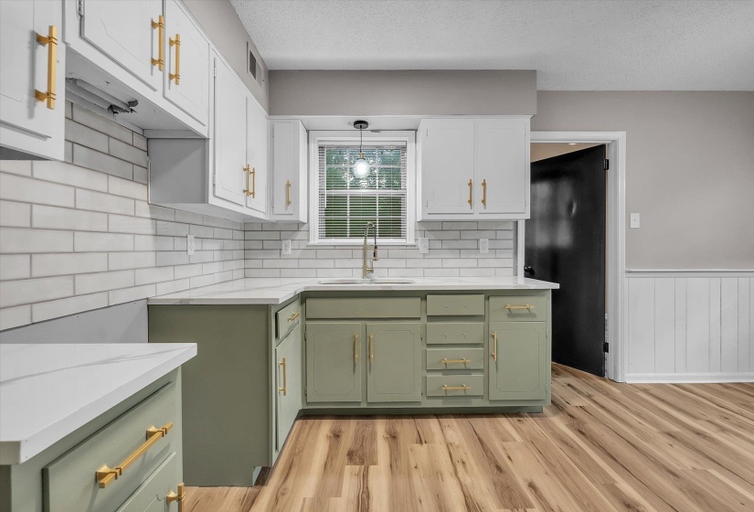 Kitchen featuring two-tone cabinetry with gold-finish hardware, white subway tile backsplash, light-toned countertops, and wood-finish flooring