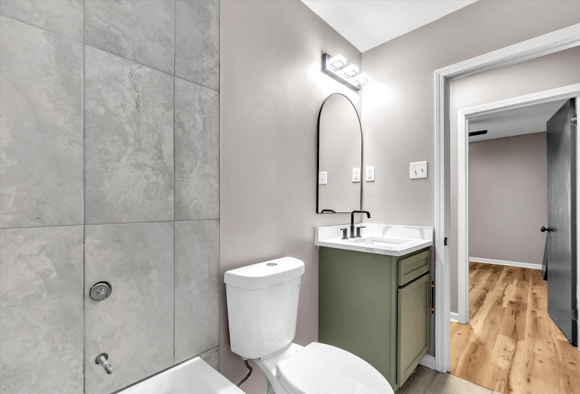 Bathroom featuring a contemporary vanity with a white countertop, a black arched mirror, and a wall-mounted light fixture