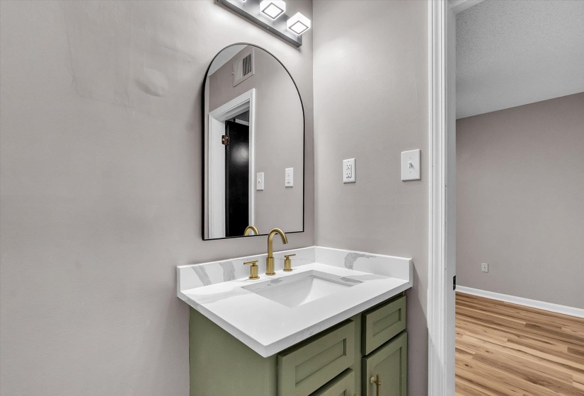 Bathroom vanity featuring a green cabinet, white countertop with integrated sink, brass-finish faucet, and an arched mirror with a black frame