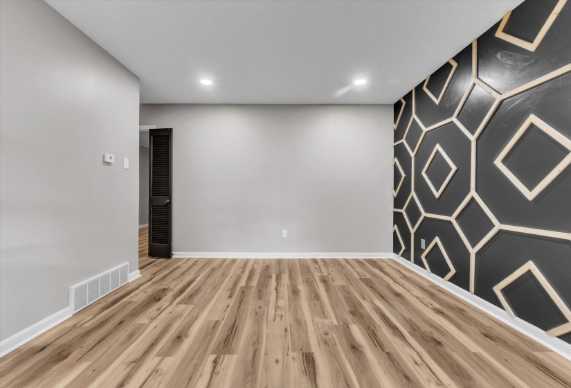 Open concept interior featuring light wood-finish flooring, recessed lighting, and a dark accent wall with a geometric pattern