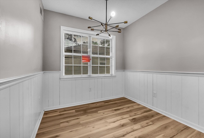 Room featuring wood-finish flooring, white wainscoting, and a modern sputnik-style chandelier