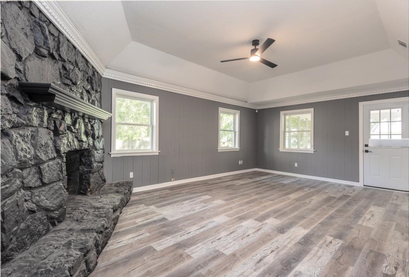 Living area featuring a stone-clad fireplace with a mantel, wood-finish flooring, and a tray ceiling with a ceiling fan